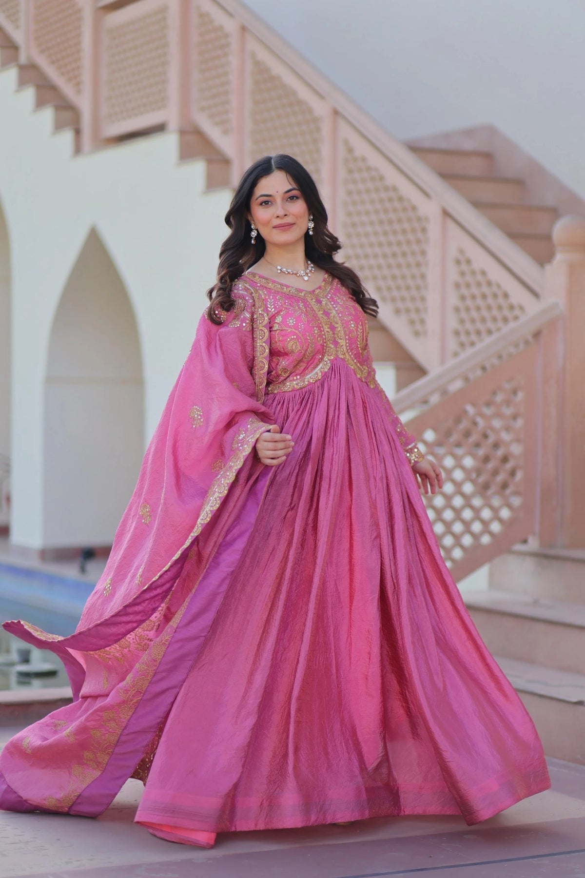 Woman in a pink traditional outfit standing in front of a decorative staircase.