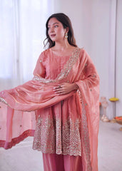 Woman wearing a pink traditional outfit with intricate embroidery in a bright room.