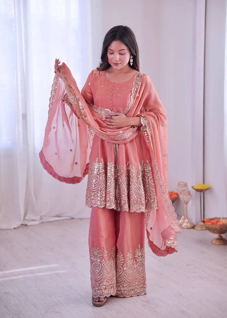 Woman in a traditional pink and gold outfit with a matching dupatta, standing indoors.