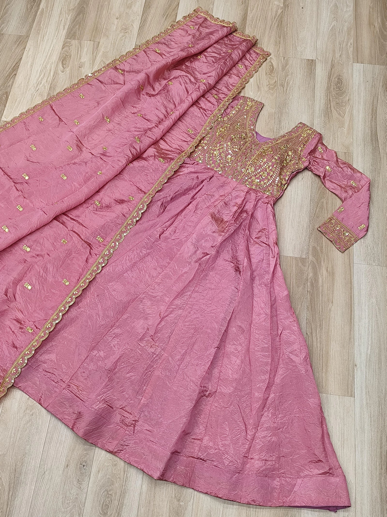 Pink traditional outfit with gold embroidery on a wooden floor
