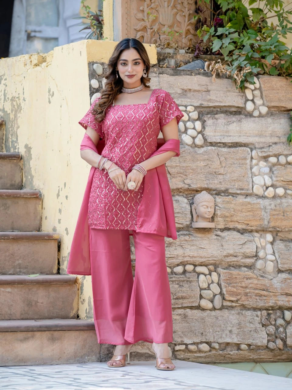 Woman in a pink traditional outfit standing on stone steps with a stone wall background