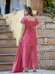 Woman in a pink outfit standing on stone steps with a stone wall and plants in the background