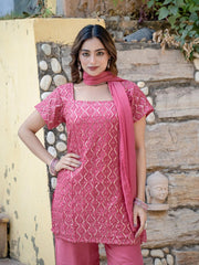 Woman wearing a pink traditional outfit with a patterned top and matching dupatta, standing against a stone wall.