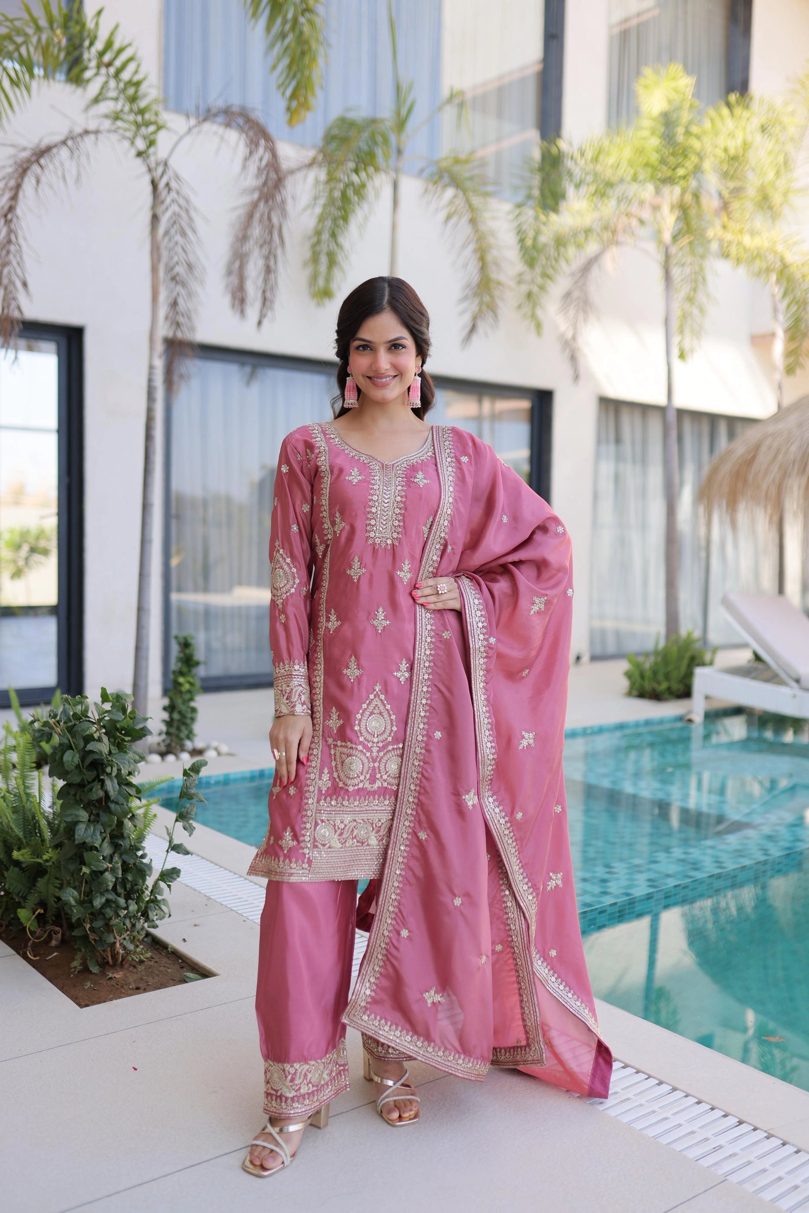 Woman in a pink traditional outfit standing by a pool with a modern building in the background