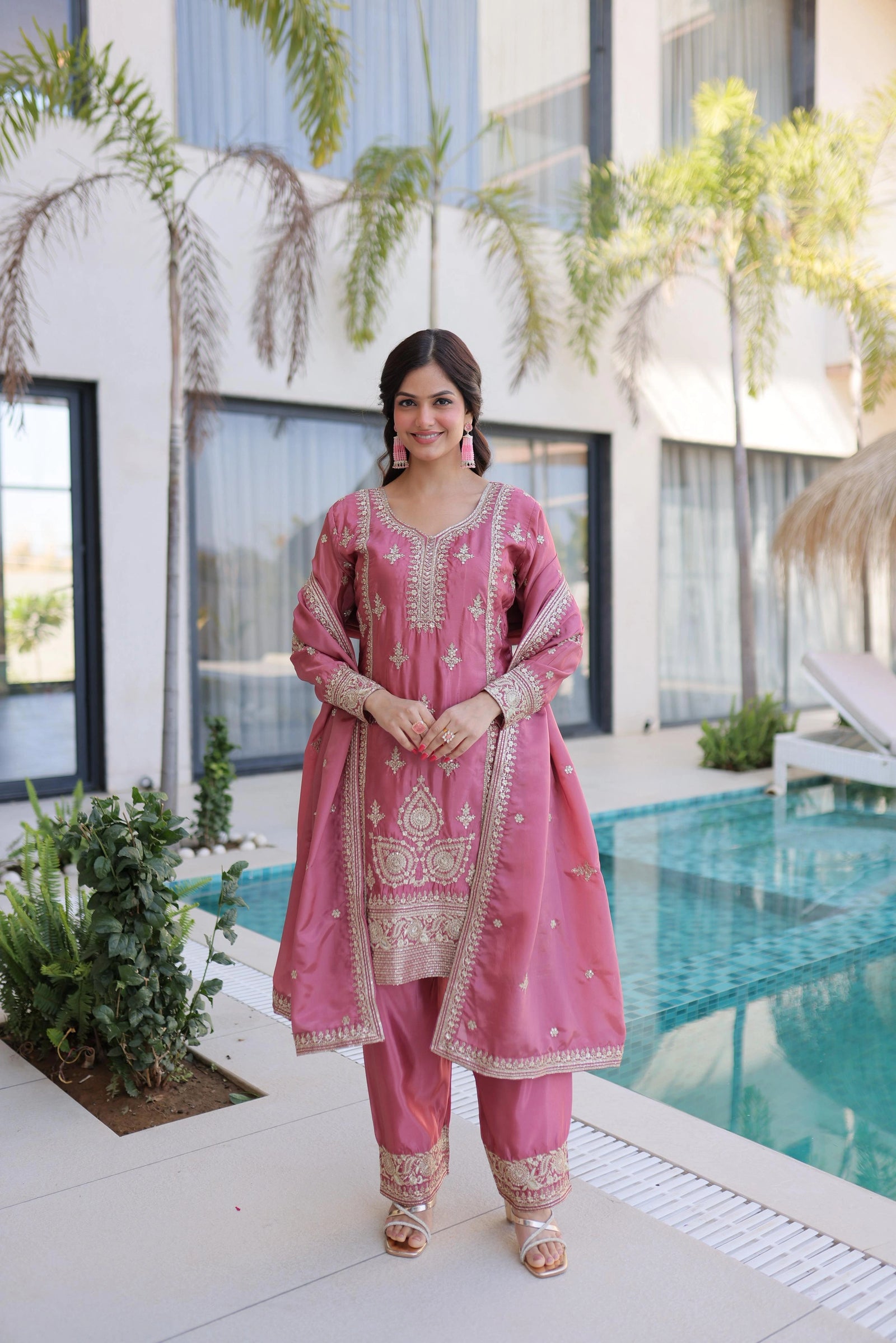 Woman in a pink traditional outfit standing by a pool with modern building and plants in the background