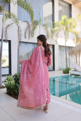 Woman in a pink traditional outfit standing by a pool with modern building and plants in the background