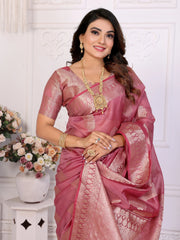 Woman in a pink saree with gold jewelry against a white wall