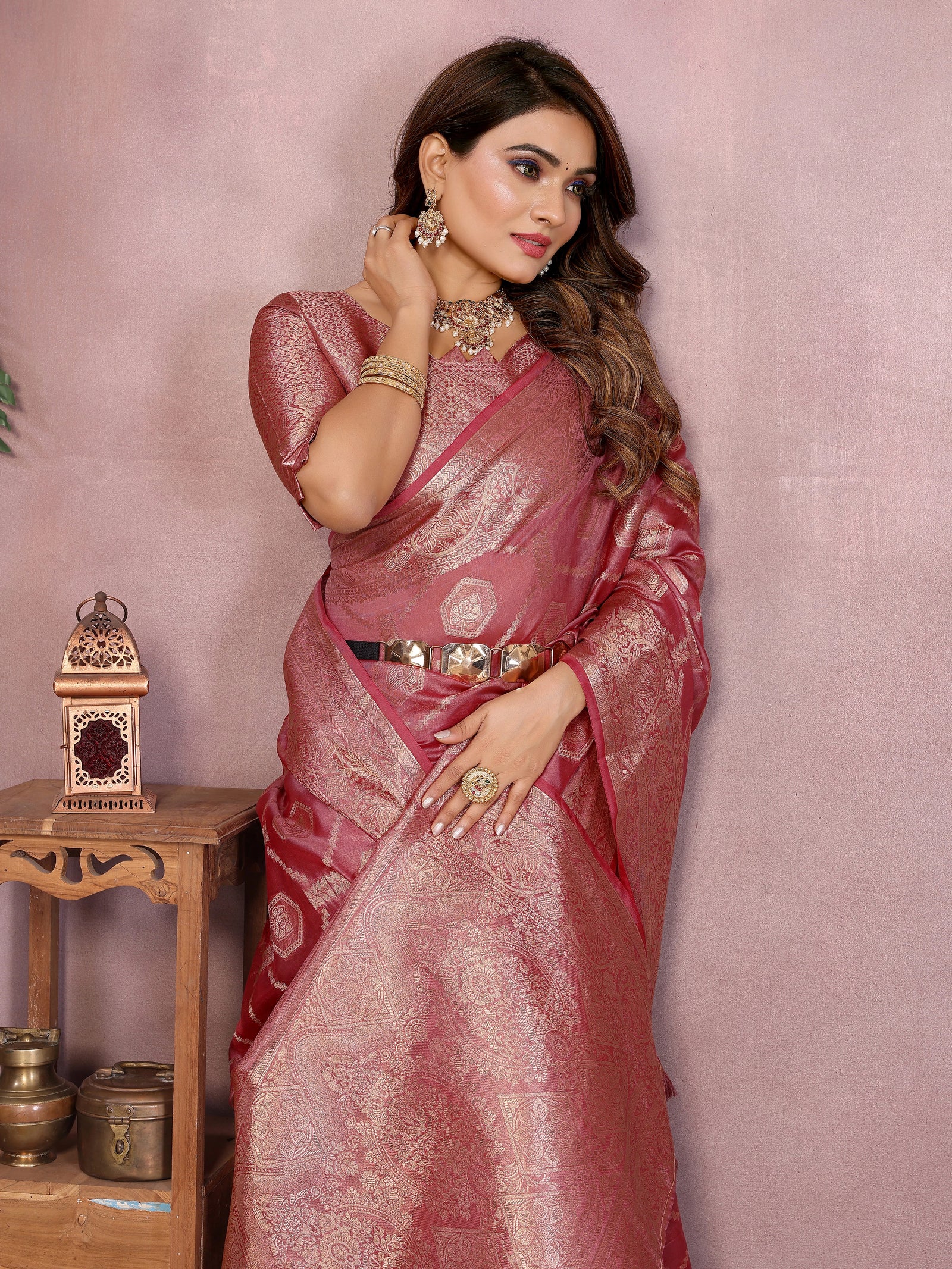 Woman in a pink saree with jewelry against a pink background