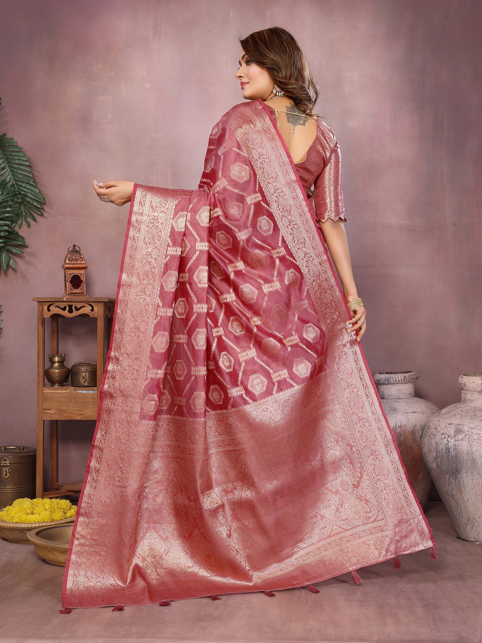Woman wearing a pink saree with a patterned border, standing against a neutral background.