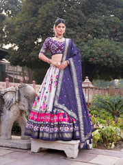 Woman in a traditional purple and pink lehenga standing outdoors with greenery in the background