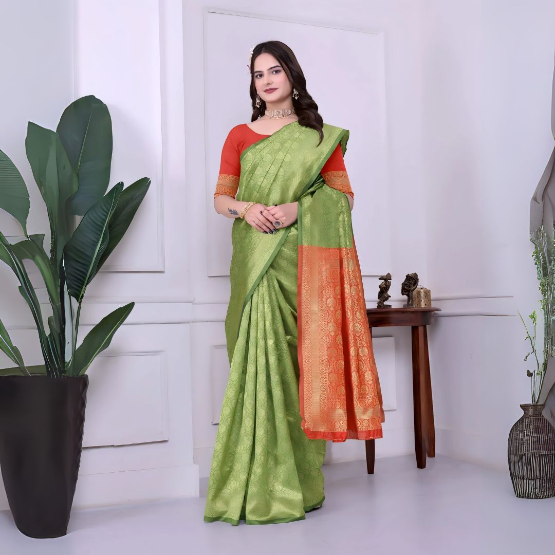 A woman models a striking Green Banarasi Silk Saree with dense tone-on-tone Zari weaving. The pallu provides a dramatic contrast in vibrant red/orange with heavy gold weaving. She wears a red/orange blouse and gold Kundan jewelry.