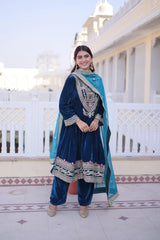 Woman in traditional blue and green outfit standing in front of a white building.