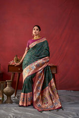 A woman models a luxurious Dark Green Soft Banarasi Silk Saree. The saree features dense, multi-colored Zari weaving across the body. The wide border and pallu showcase heavy gold Zari work with prominent blue and purple accents. She wears a contrasting purple blouse and a heavy gold Kundan choker necklace, posing indoors.