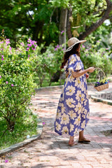 Woman in a floral dress and sun hat walking through a garden