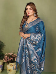 Woman wearing a blue saree with intricate patterns against a green background