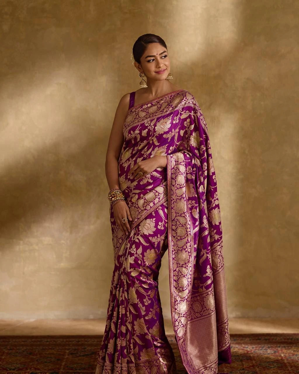 Woman wearing a purple saree with gold patterns against a beige background