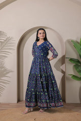 Woman wearing a blue floral dress standing in front of an archway with plants.