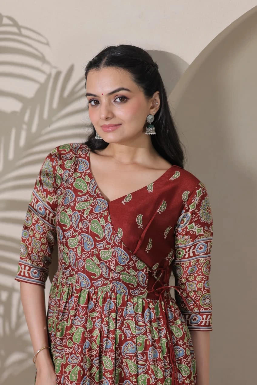 Woman wearing a patterned dress standing against a neutral wall.