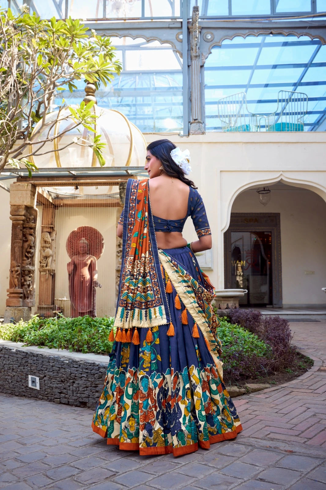 Woman in a colorful traditional outfit standing in an outdoor setting with architectural elements.