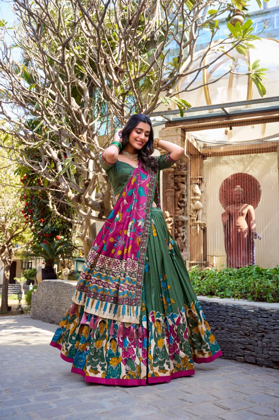Woman in a colorful traditional outfit standing outdoors with trees and a building in the background