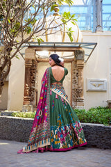 Woman in a traditional green and multicolored saree standing outdoors with decorative elements in the background.