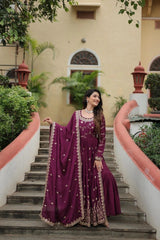 Woman in a purple traditional outfit standing on a staircase with greenery and a building in the background