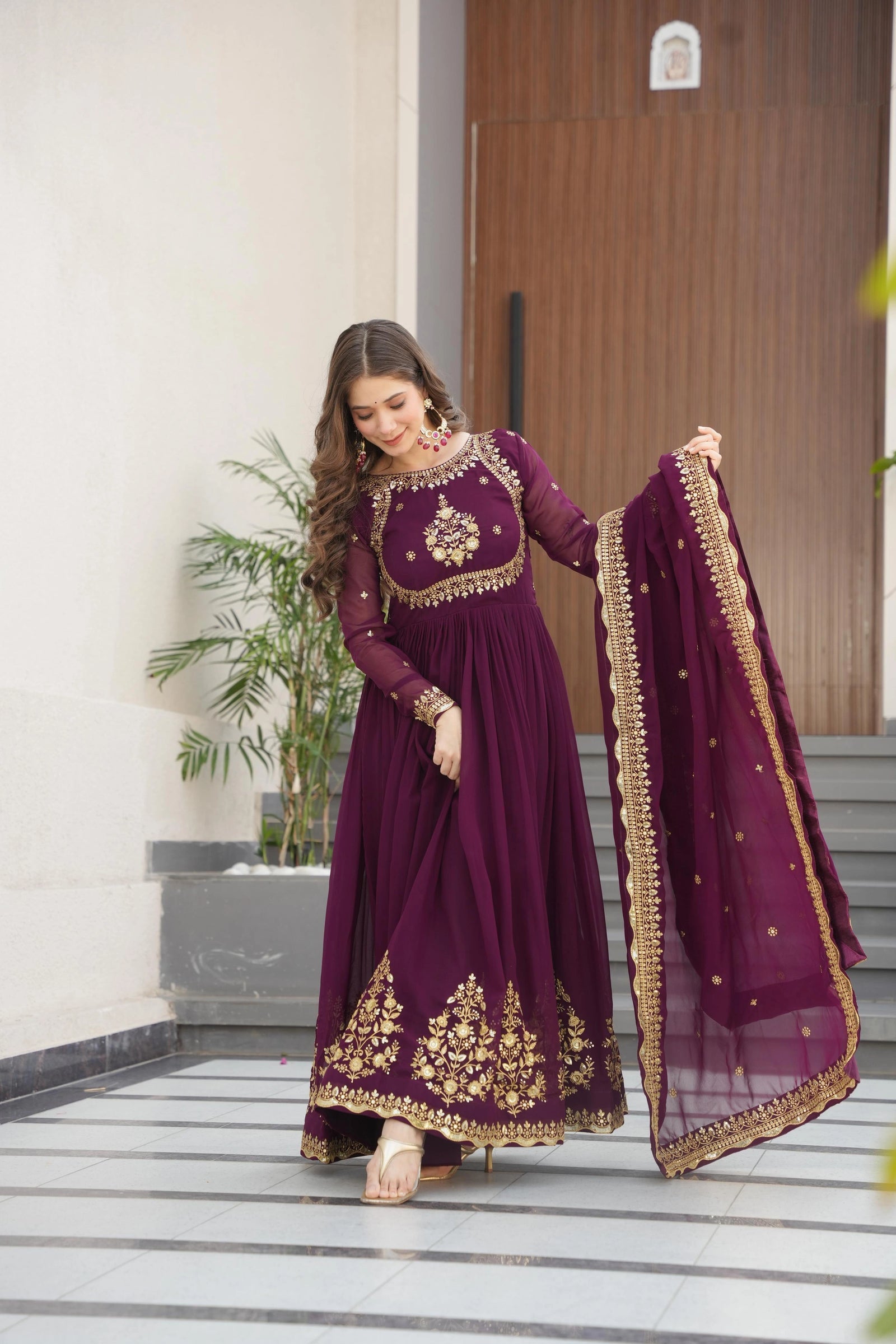 Woman in a purple traditional outfit with gold embroidery standing on a staircase.