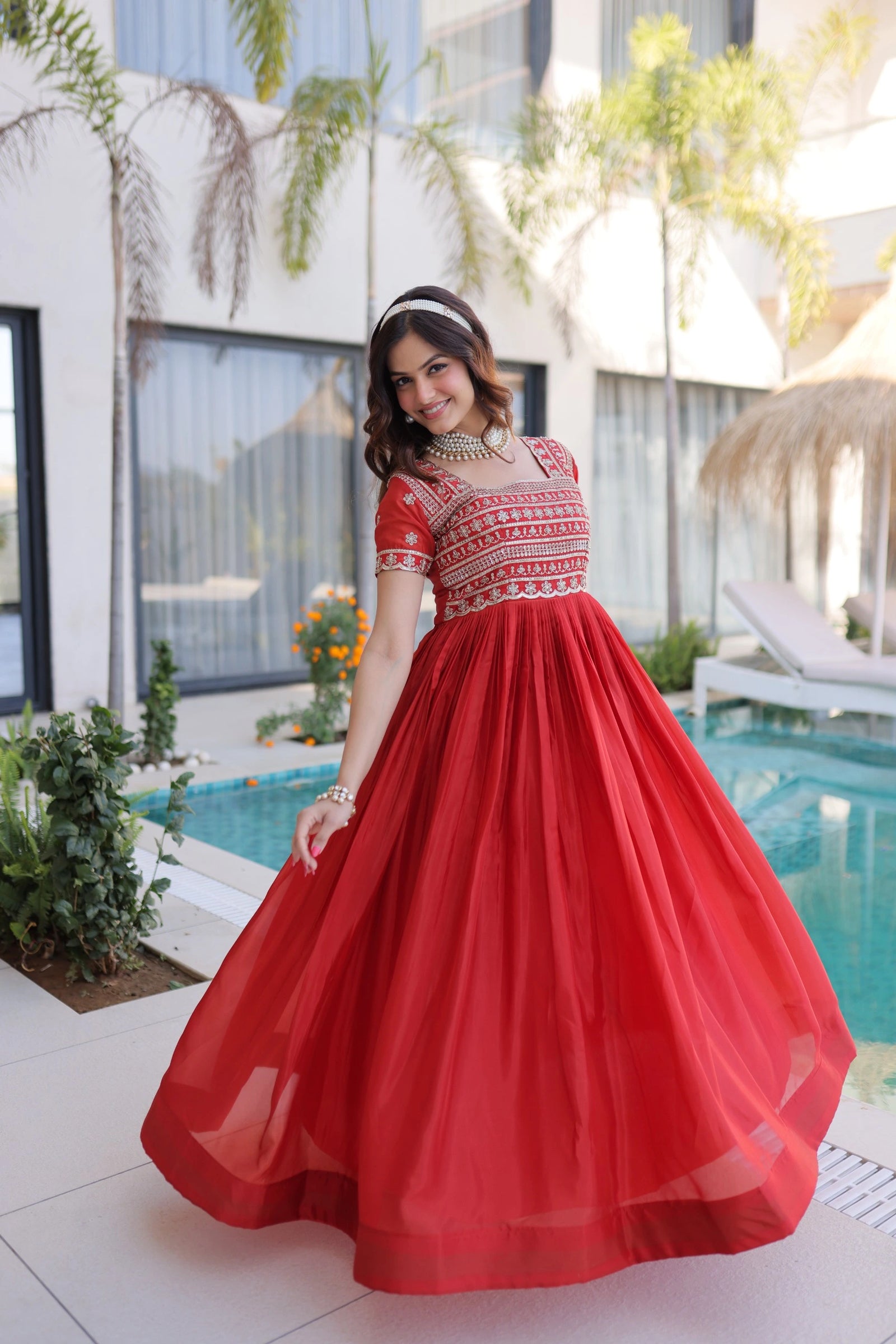 Woman in a red dress standing by a pool with a modern building in the background