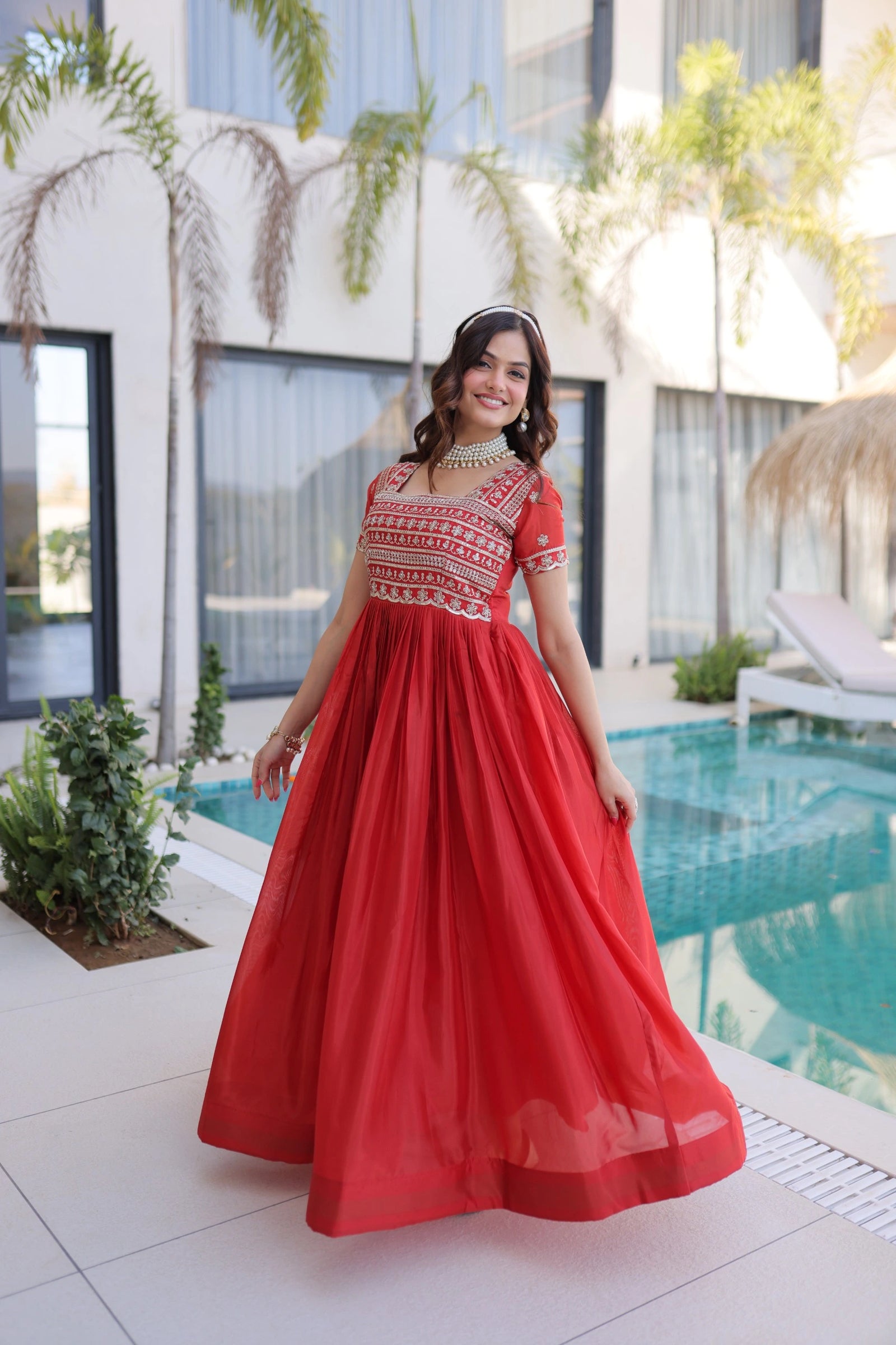 Woman in a red dress standing by a pool with plants and a building in the background