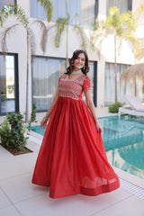 Woman in a red dress standing by a pool with plants and a building in the background