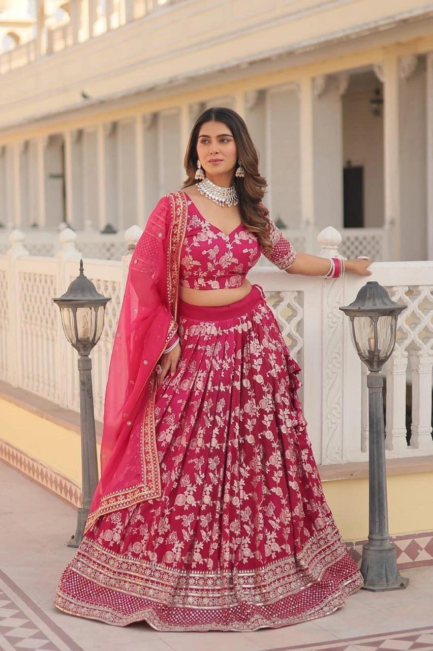 Woman in a traditional pink and red lehenga standing in front of a decorative building.