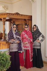 Three women in traditional attire standing indoors with a wooden structure and decorative elements in the background.