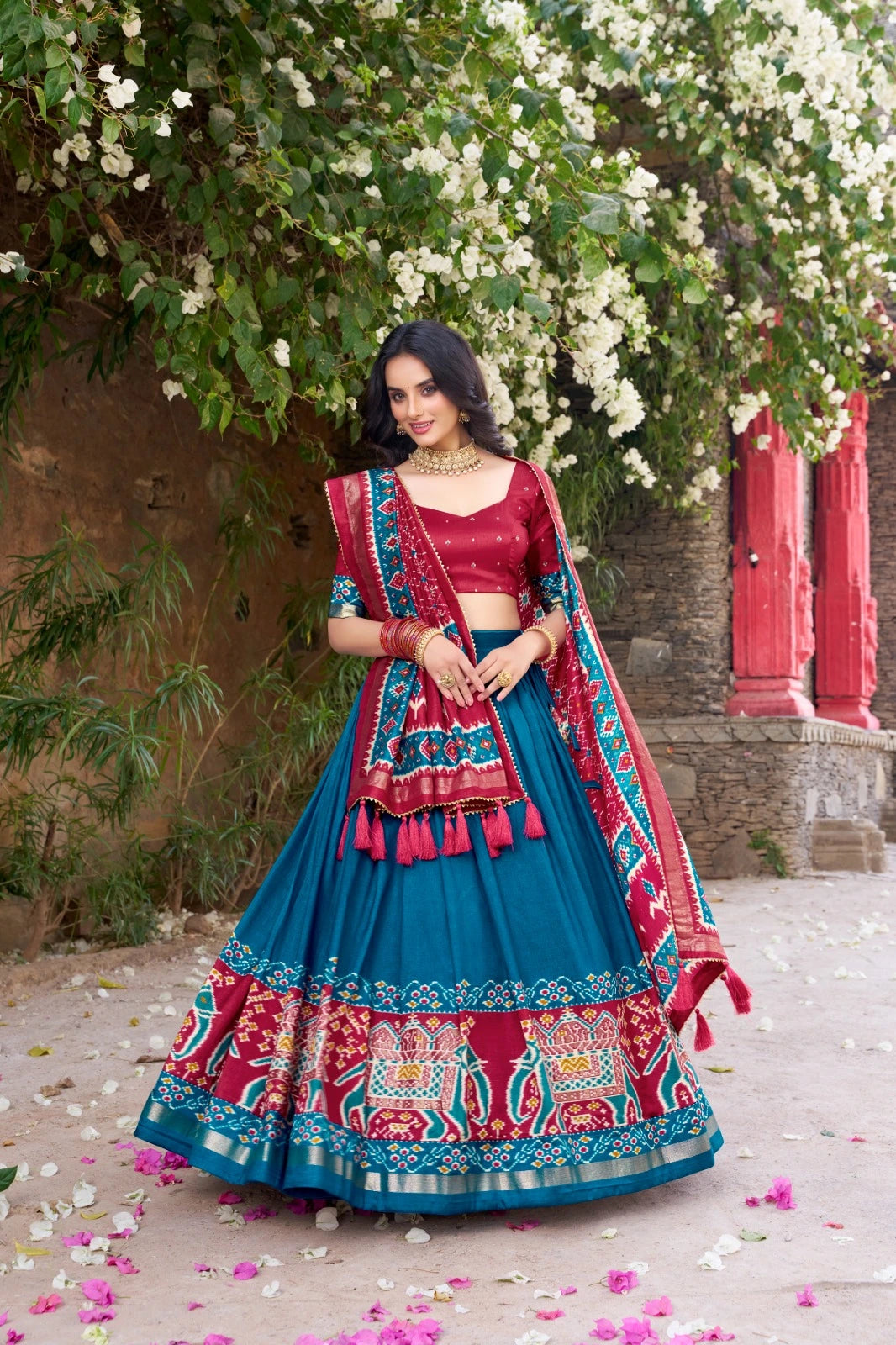Woman in a traditional blue and red outfit standing under a floral archway.