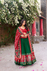 Woman in a red and green traditional outfit standing in front of a building with white flowers.