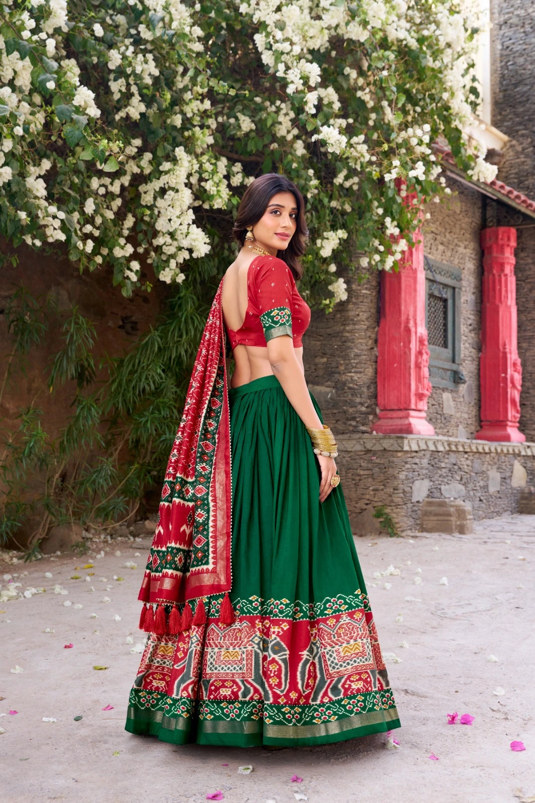 Woman in a traditional green and red outfit standing in front of a floral backdrop