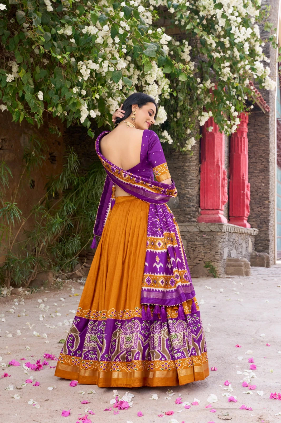 Woman in a purple and yellow traditional outfit standing under a floral archway.