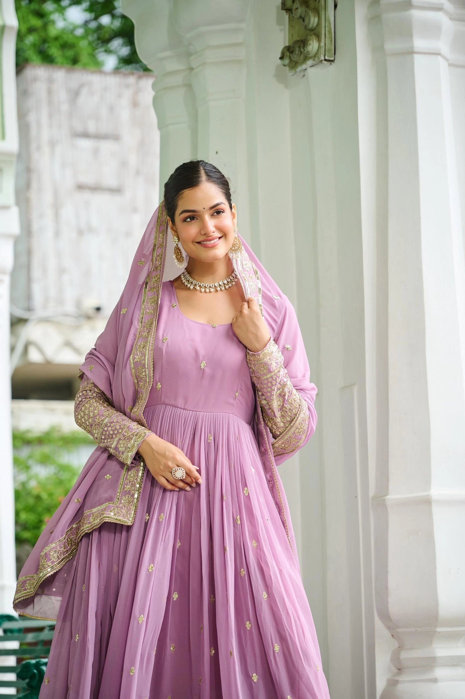 Woman in a pink traditional outfit with gold embroidery standing outdoors.