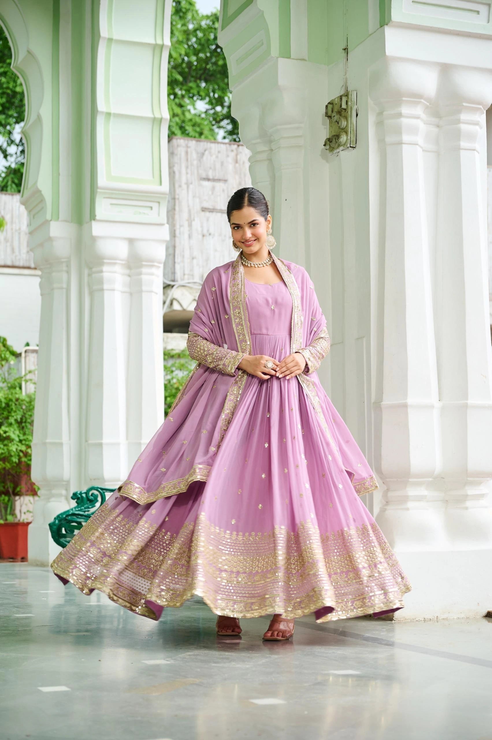 Woman in a pink traditional outfit standing in a decorative indoor setting.
