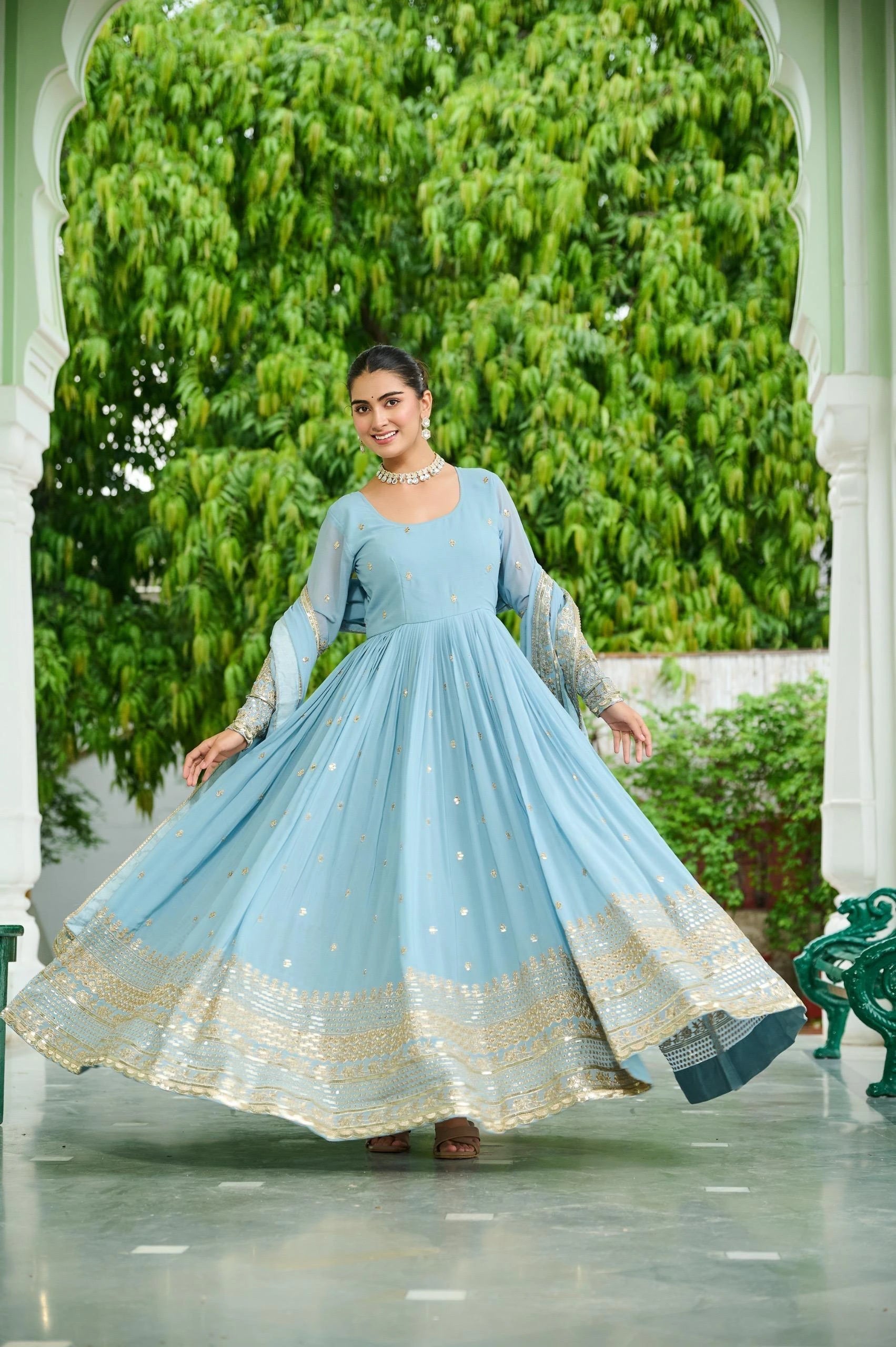Woman in a light blue traditional outfit standing in front of greenery
