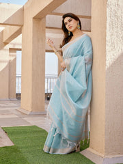 Woman in a light blue saree standing against a beige architectural background