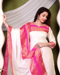 Woman wearing a white saree with pink and gold border against a green background