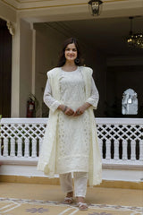 Woman in a white traditional outfit standing in a decorative indoor setting.