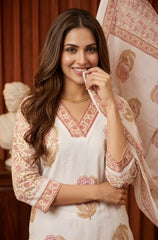 Woman wearing a white and pink embroidered traditional outfit with a decorative scarf.