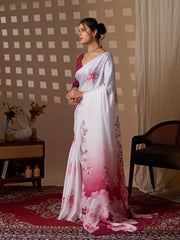 Woman in a white saree with pink floral patterns standing in a room with a checkered wall and wooden furniture.