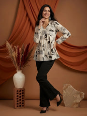 Woman wearing a black and white patterned top with black pants against a brown curtain background.