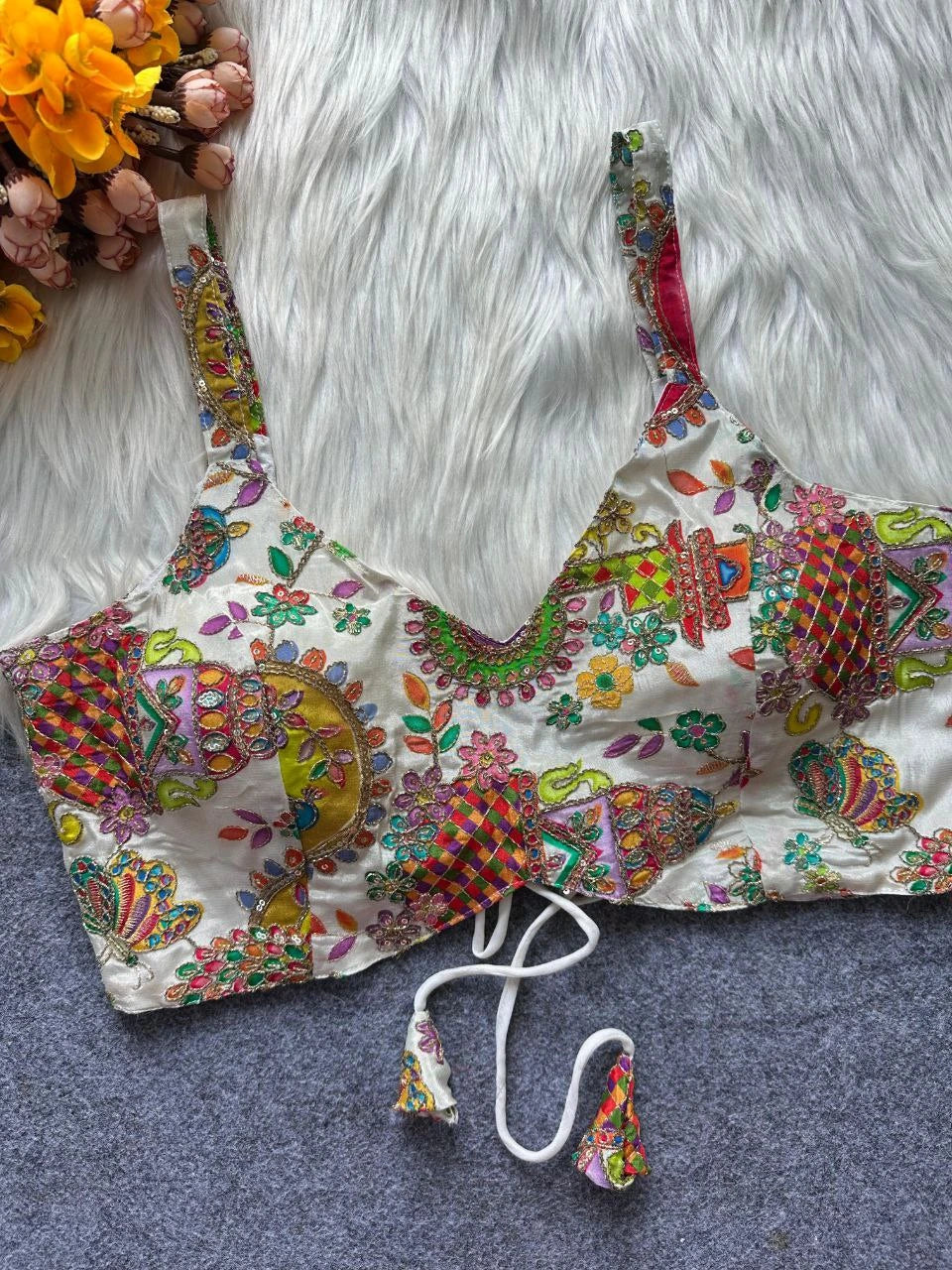Colorful embroidered bralette on a textured surface with flowers in the background