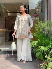 Woman in traditional outfit standing outdoors with plants in the background