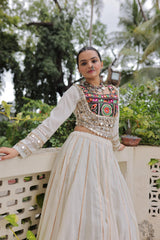 Woman in traditional outfit with embroidered top and white skirt standing outdoors.