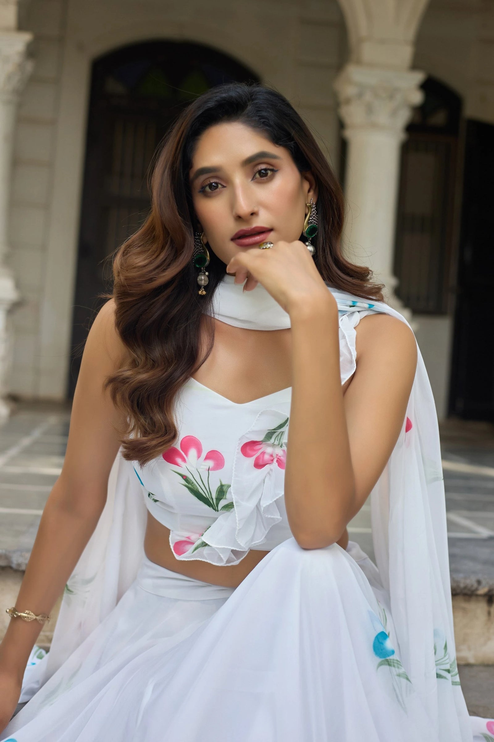 Woman in a white floral outfit sitting outdoors with classical architecture in the background
