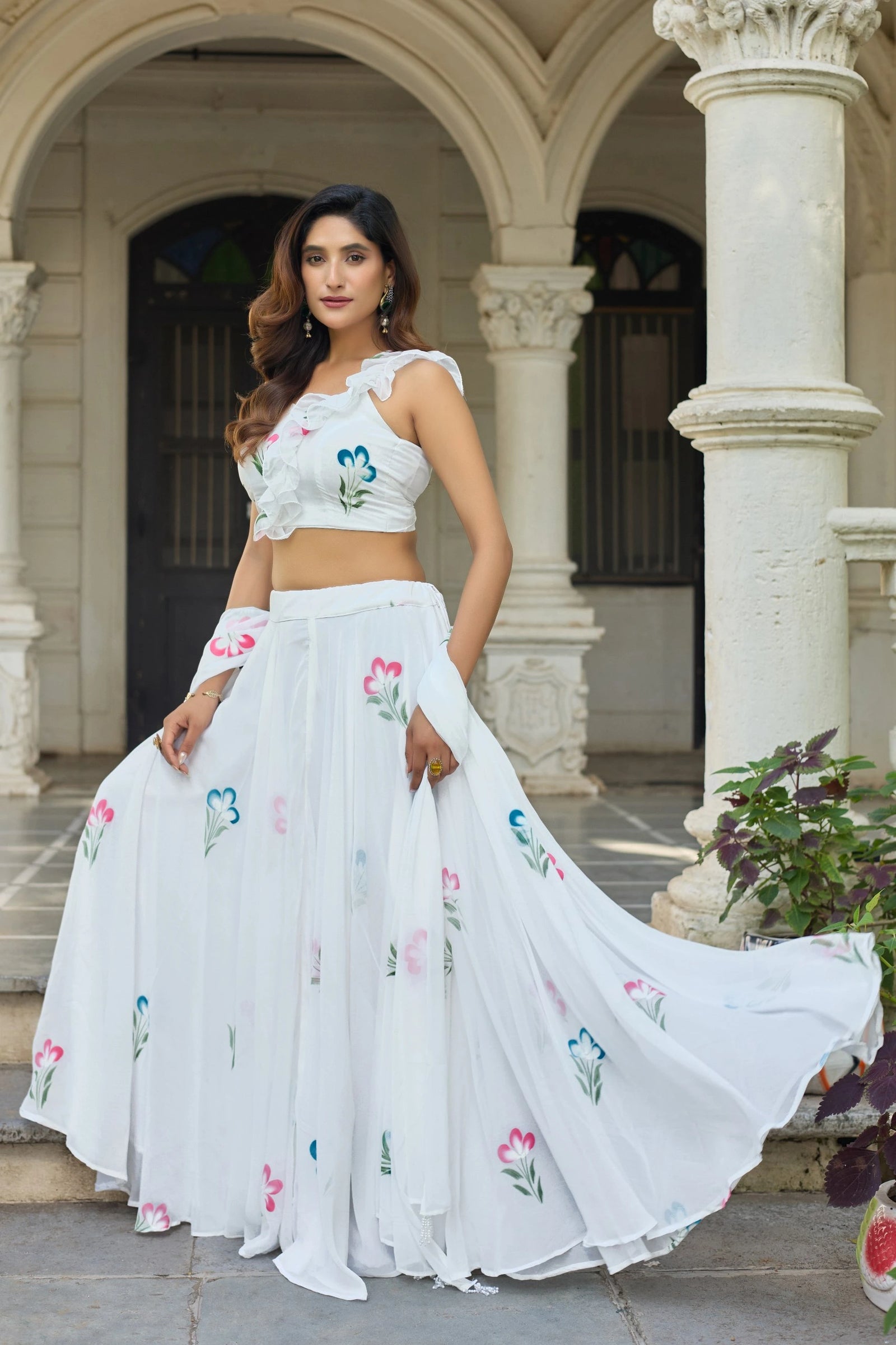 Woman in a white embroidered outfit standing in front of classical architecture.